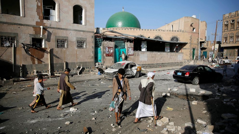 FILE - In this Sept. 3, 2015, file photo people walk at the site of a car bomb attack next to a Shiite mosque in Sanaa, Yemen. Yemen’s civil war has exacted an enormous toll on people with disabilities, who find themselves on the margins of society a