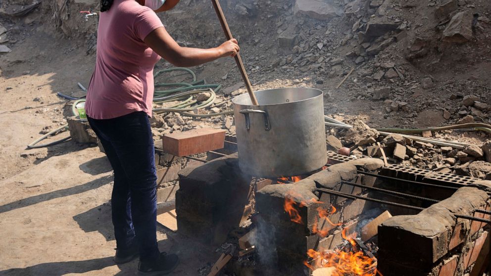 Cindy Cueto stirs a large pot of rice over an open fire at the San Miguel or Michael the Archangel soup kitchen in the Villa Maria neighborhood of Lima, Peru, Tuesday, April 12, 2022. Community soup kitchens are once again on the rise as a lifeline f