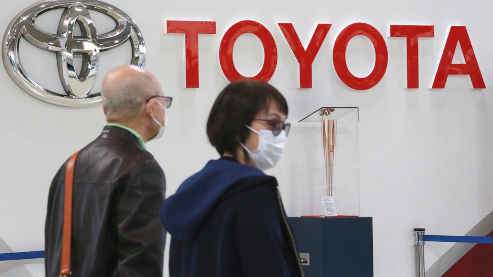 FILE - People walk past the logo of Toyota at a showroom in Tokyo, Monday, Oct. 18, 2021. Toyota is suspending production at all 28 lines of its 14 plants in Japan starting Tuesday, because of a “system malfunction” at a domestic supplier, the automa