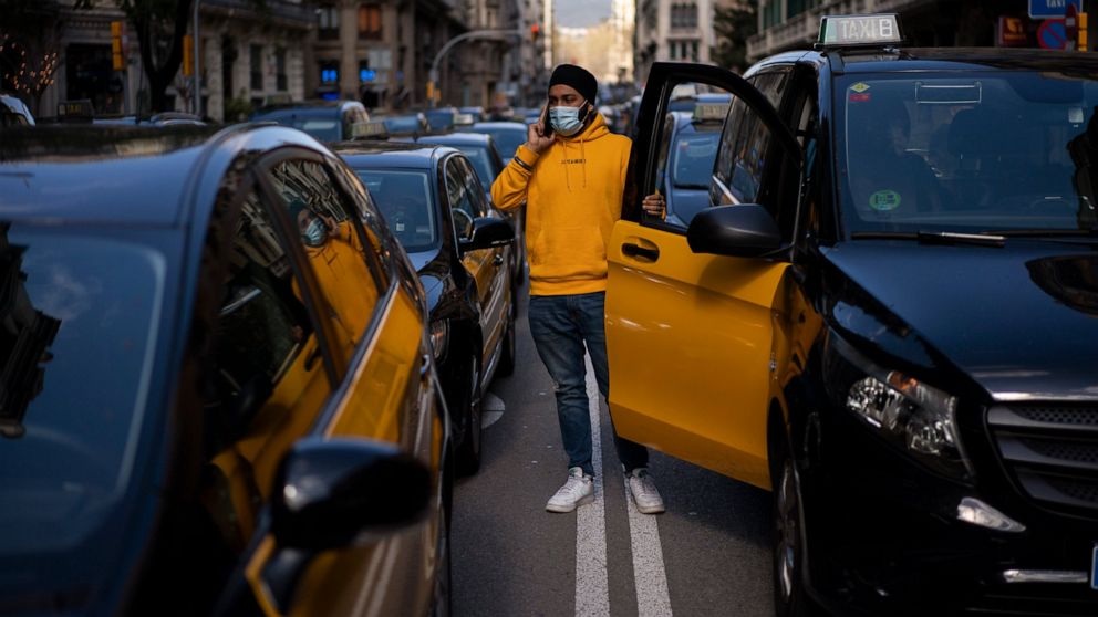 A taxi driver stands next to his cab as they march slowly blocking the traffic along one of the avenues in Barcelona downtown, Spain, Thursday, March 18, 2021. Hundreds of yellow-and-black cabs disrupted Barcelona's road traffic on Thursday to protes