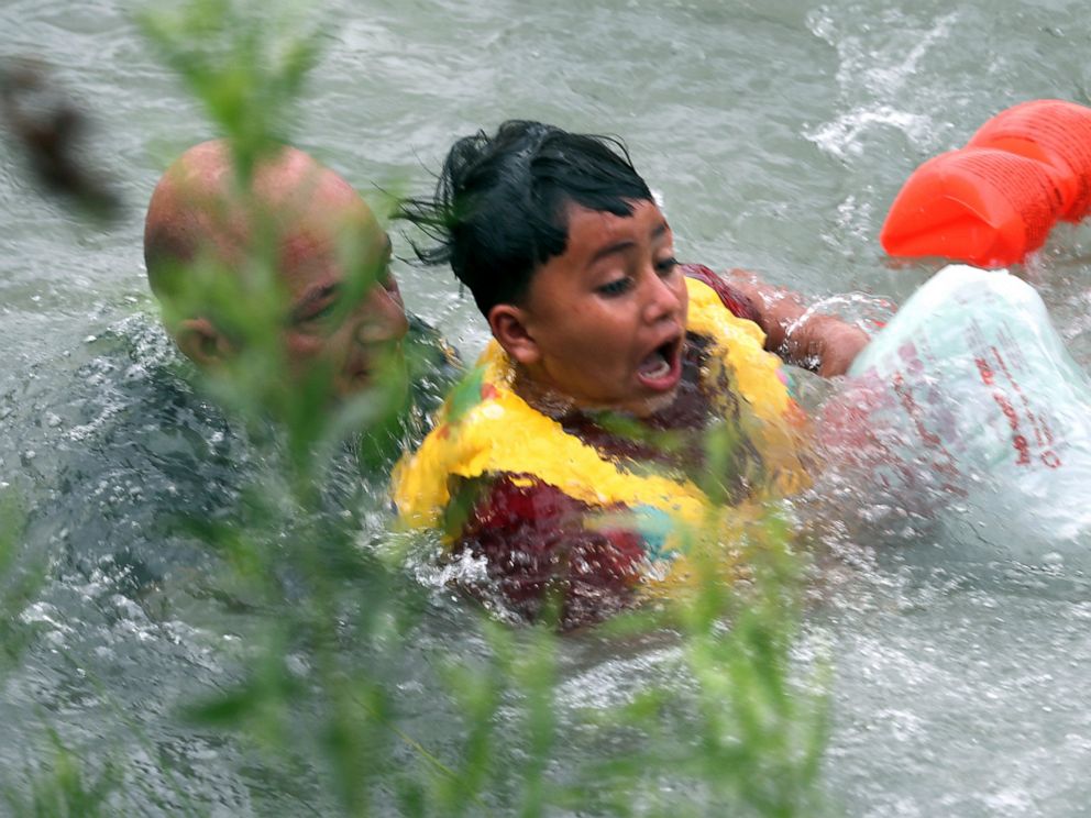 In this Friday, May 10, 2019 photo, Border Patrol Agent Brady Waikel rescues a 7-year-old boy from Honduras after he fell out of a makeshift raft and lost hold of his mother as Border Patrol agents respond to rafts crossing the Rio Grande River near