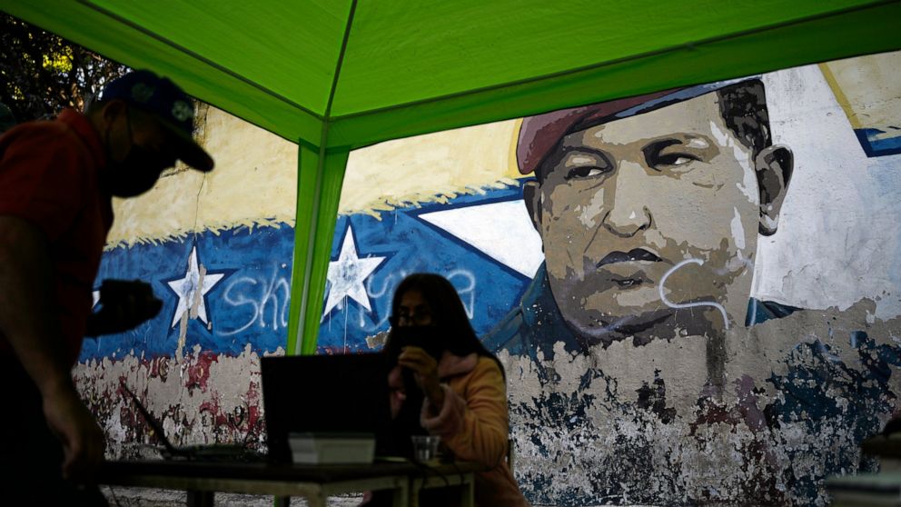 A mural of late President Hugo Chavez decorates a street wall where a table is set up, by the National Election Council (CNE), where people can sign a petition in favor of holding a referendum to remove President Nicolas Maduro from office in Caracas