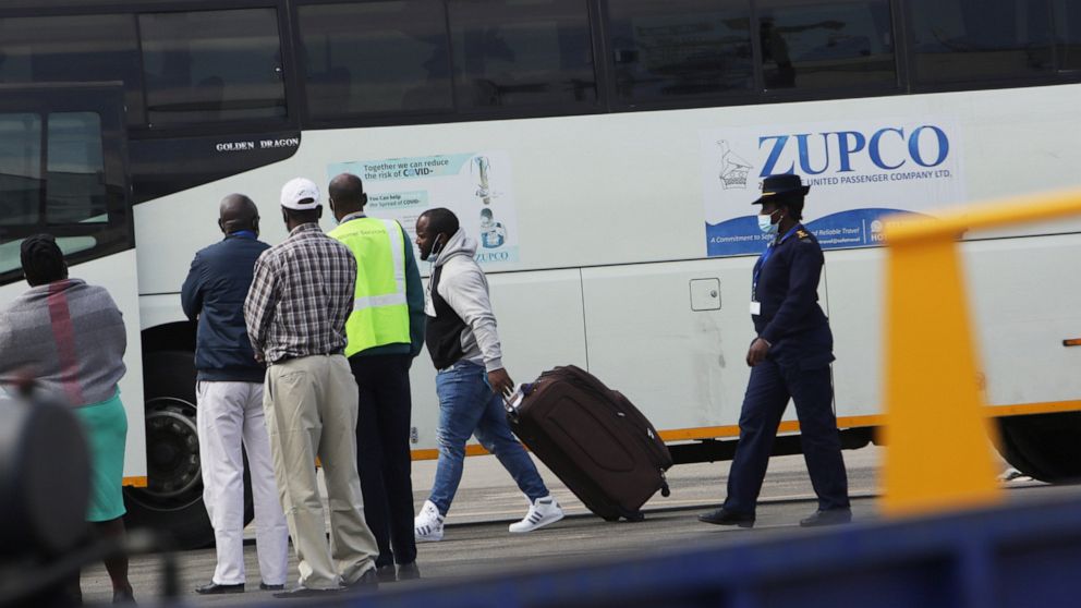 A Zimbabwean National, centre, is escorted to the bus by a police upon his arrival upon arrival at Robert Mugabe International airport in Harare, Thursday, July 22, 2021. Zimbabwe has received the first batch of dozens of its citizens being deported 