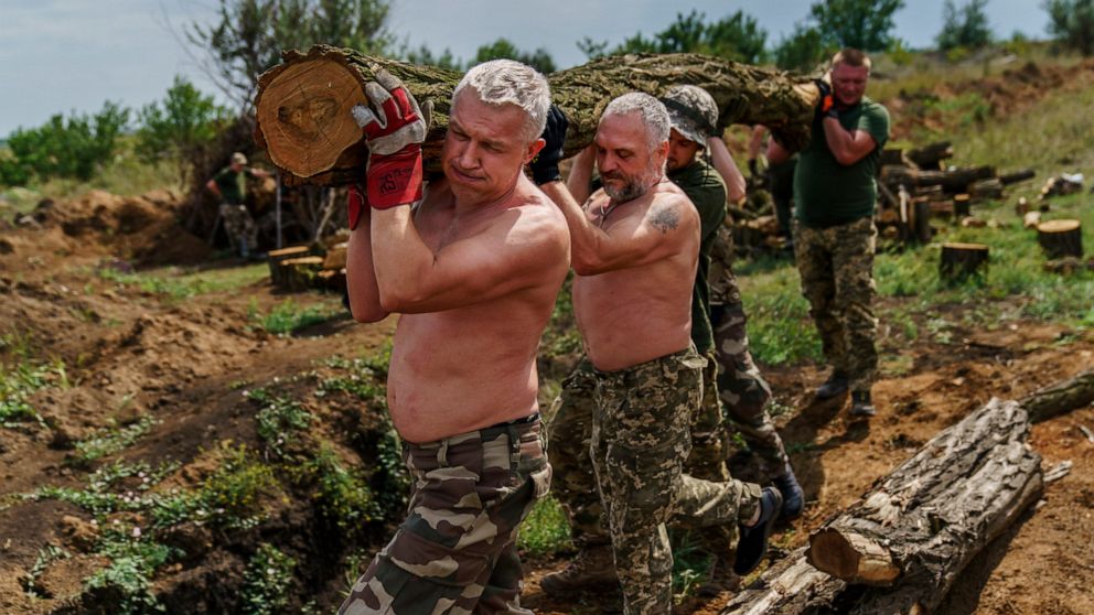 Members of the Dnipro-1 regiment carry logs to fortify their position near Sloviansk, Donetsk region, eastern Ukraine, Friday, Aug. 5, 2022. While the lull in rocket strikes has offered a reprieve to remaining residents, some members of the Ukrainian