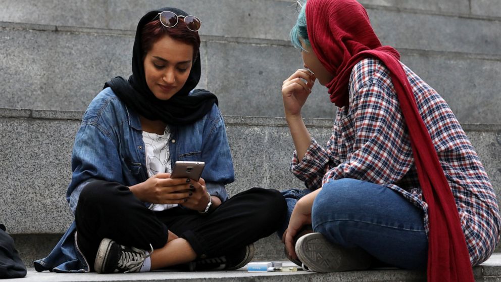 In this Tuesday, July 2, 2019 photo, an Iranian woman works on her cell phone while spending an afternoon on steps outside of a shopping mall in northern Tehran, Iran. Before Iranians can check out the latest offerings on Twitter or YouTube, they mus