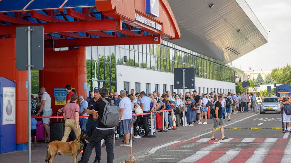Security personnel and an explosive sniffing dog stand at the entrance of the departures terminal as passengers wait in line at the international airport in Chisinau, Moldova, Tuesday, Aug. 16, 2022. Over the last two months non-European Union Moldov