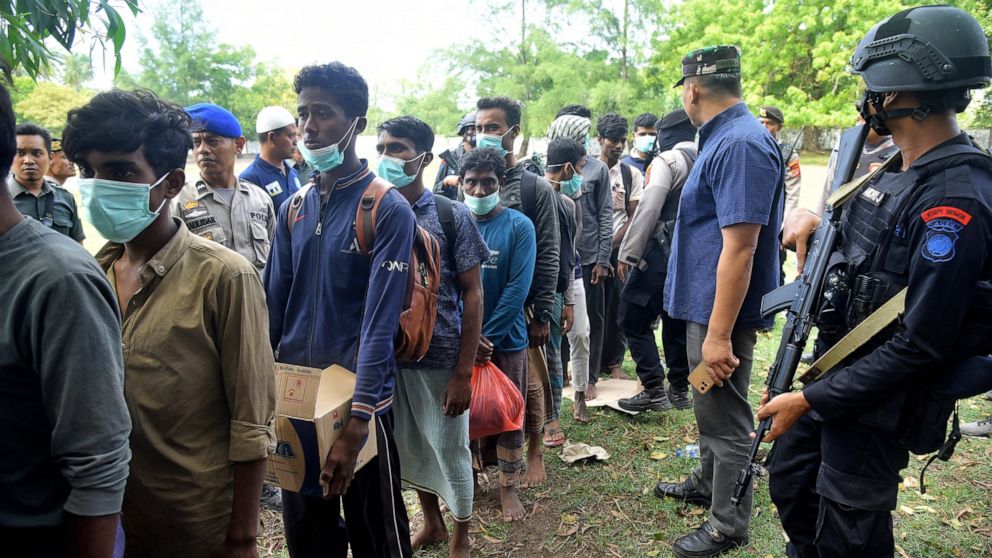 Security officers stand by Rohingya refugees after they arrived on Indra Patra beach in Ladong village, Aceh province, Indonesia, Sunday, Dec. 25, 2022. Dozens of hungry and weak Rohingya Muslims were found on a beach in Indonesia's northernmost prov