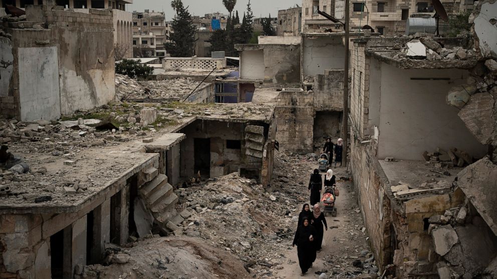 In this Thursday, March 12, 2020 photo, women walk in a neighborhood heavily damaged by airstrikes in Idlib, Syria. Idlib city is the last urban area still under opposition control in Syria, located in a shrinking rebel enclave in the northwestern pr