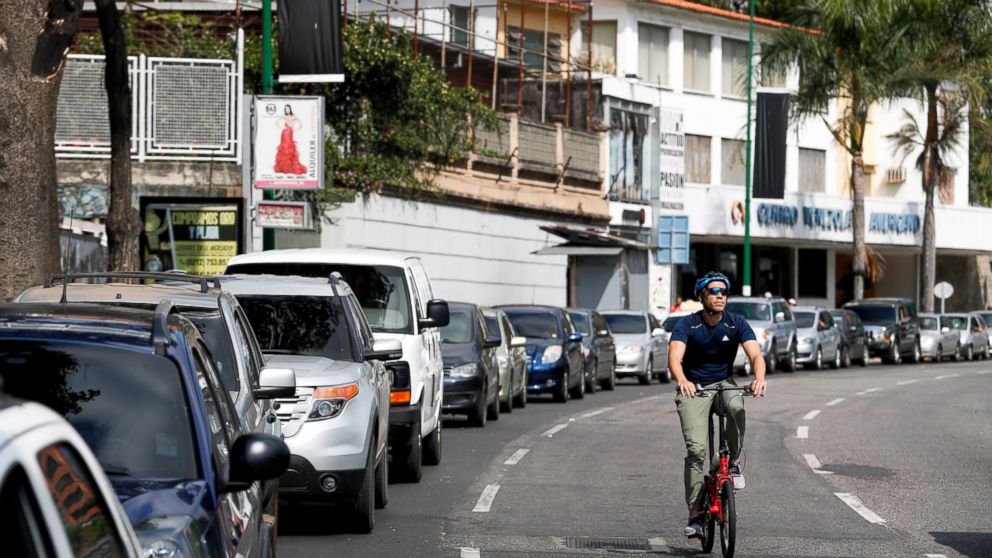 A cyclist pedals through an empty street, past motorists waiting to fill up at one of the few fuel stations that has electricity, during rolling blackouts in Caracas, Venezuela, Sunday, March 10, 2019. Power and communications outages continue to hit
