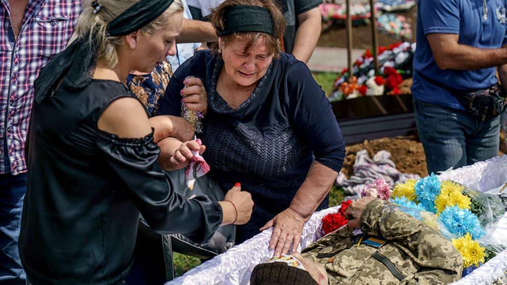 Lilia Panchenko, right, is pulled away as she says her final goodbye to her son, Oleh, along with his daughter, Ruslana, before his casket is covered during his burial service in Pokrovsk, Donetsk region, eastern Ukraine, Thursday, Aug. 4, 2022. Panc
