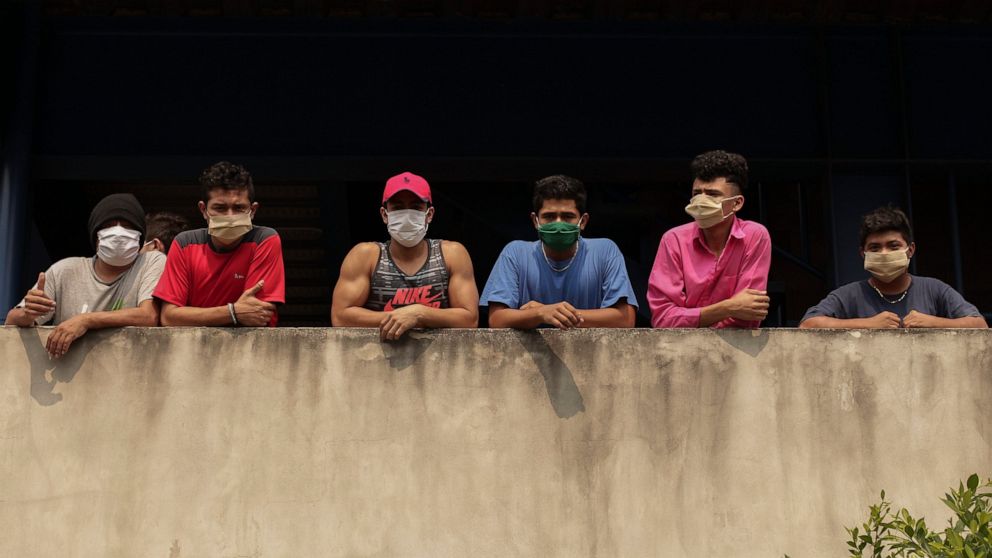 In this May 4, 2020 photo, men wearing protective face masks look out from a building where they are being held for violating a quarantine decreed by the government as part of measures to curb the spread of COVID-19, in San Salvador, El Salvador. The