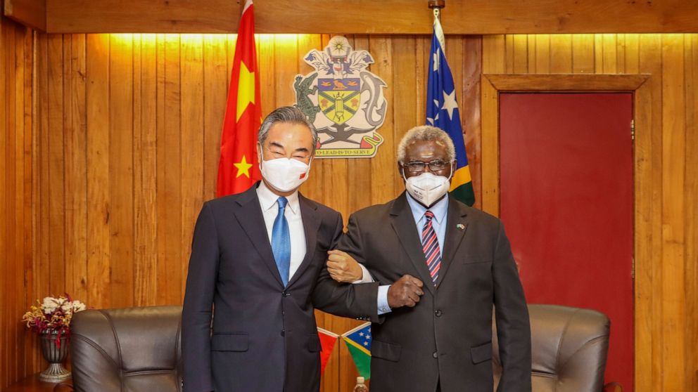 In this photo released by Xinhua News Agency, Solomon Islands Prime Minister Manasseh Sogavare at right lock arms with visiting Chinese Foreign Minister Wang Yi in Honiara, Solomon Islands, Thursday, May 26, 2022. (Xinhua via AP)