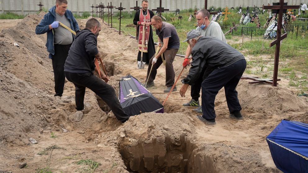 Workers put into a grave a coffin with unidentified remains of a civilian murdered by the Russian troops during Russian occupation in Bucha, on the outskirts of Kyiv, Ukraine, Thursday, Aug. 11, 2022. Eleven unidentified bodies exhumed from a mass gr