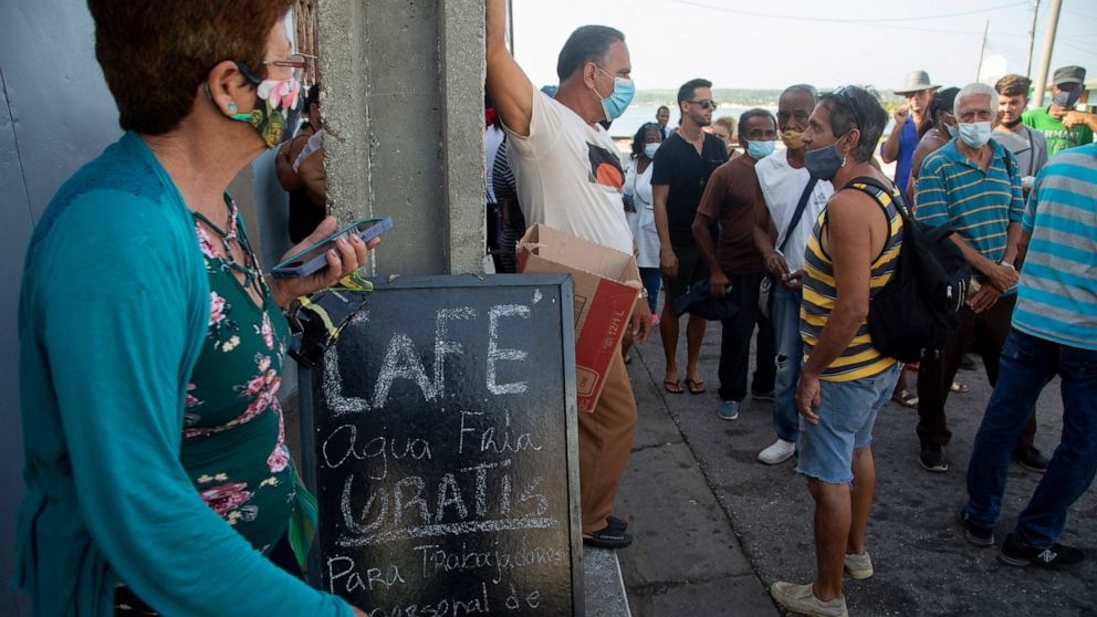 Residents wait in line to buy groceries next door to a coffee shop that has a sign announcing free coffee and water for those working to extinguish a deadly fire at a large oil storage facility in Matanzas, Cuba, Tuesday, Aug. 9, 2022. The fire was t