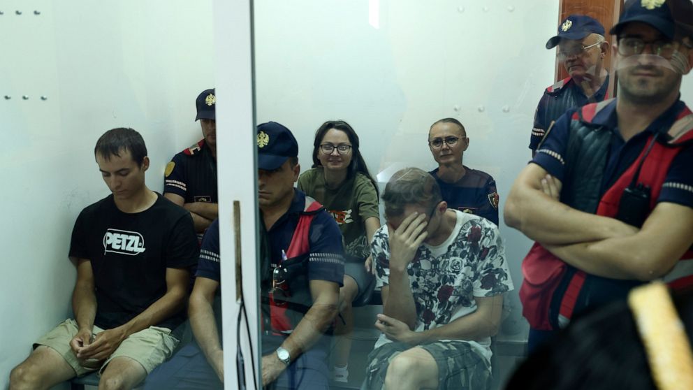 Russian Mikhail Zorin, left, Russian Svetlana Timofeeva, background, and Ukrainian Fedir Alpatov, right, guarded by policemen appear at a court in Elbasan, Albania, Wednesday, Aug. 24, 2022. The two Russians and the Ukrainian were arrested for allege