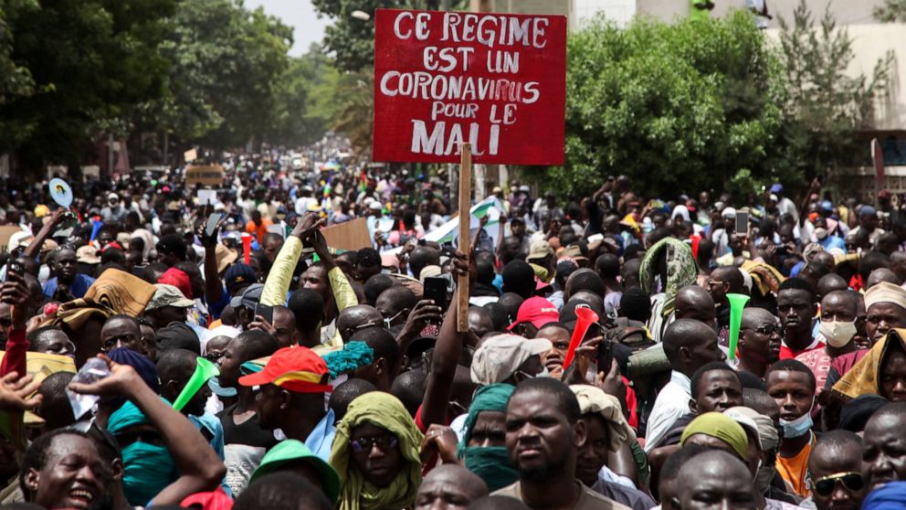 Demonstrators hold a placard in French reading "This regime is a coronavirus for Mali" as they protest in the capital Bamako, Mali Friday, June 5, 2020. Thousands of people demonstrated in Mali's capital on Friday to demand the resignation of Preside
