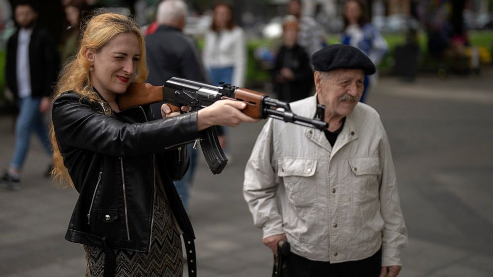 A woman uses a plastic Kalashnikov rifle to shoot balls at a portrait of Russian President Vladimir Putin, at a street attraction in the centre of Lviv, Ukraine on Saturday, May 14, 2022. (AP Photo/Emilio Morenatti)