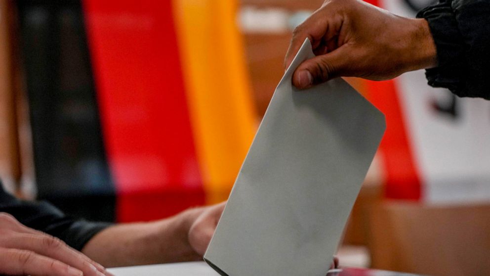 A man casts his ballot for the German elections in a polling station in Berlin, Germany, Sunday, Sept. 26, 2021. In background the German national flag. (AP Photo/Michael Probst)