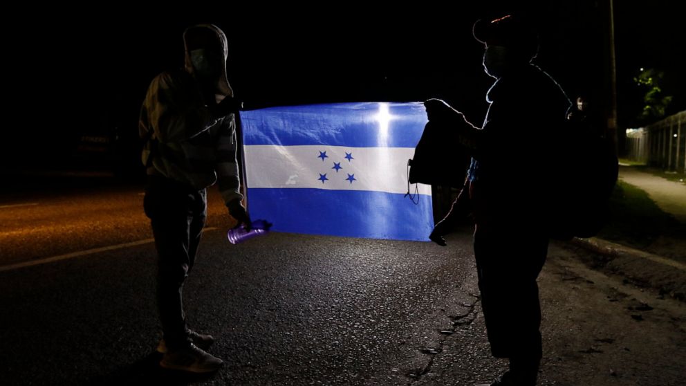 Members of a migrant caravan hold a Honduran national flag as they begin their journey in the hopes of reaching the United States, in San Pedro Sula, Honduras, Saturday, Jan. 15, 2022. (AP Photo/Delmer Martinez)