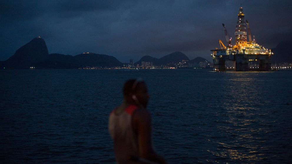 FILE - In this April 21, 2015 file photo, a man fishes near a floating oil platform in Guanabara Bay in Niteroi, Brazil. The administration of Jair Bolsonaro plans to auction seven oil fields despite contrary advice from analysts of Brazil's main env