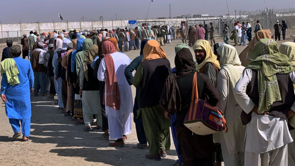 Afghan and Pakistani nationals stand in a queue and wait their turn to enter into Afghanistan through a border crossing point, in Chaman, Pakistan, Saturday, Aug. 21, 2021. (AP Photo)