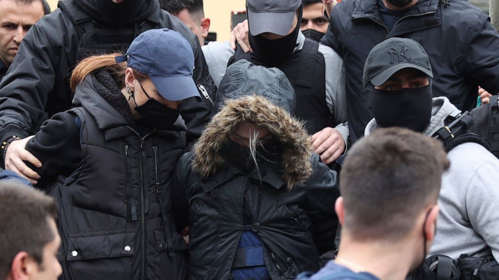 A 33-year-old woman, center with the hooded jacket, is escorted by police as she leaves the court in Athens, Greece, Thursday, March 31, 2022. The woman from Patras city, southern Greece, has been charged with the murder of her 9-year-old daughter, f