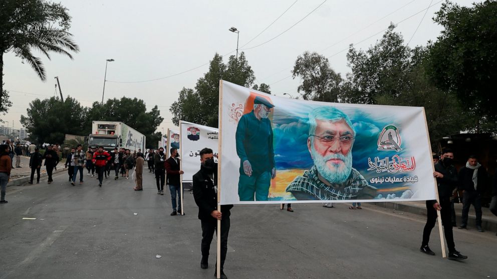 Supporters and members of the Popular Mobilization Forces hold posters of a powerful Iranian general and a top Iraqi militia leader in Baghdad, Iraq, Saturday, Jan. 1, 2022. Hundreds rally in Baghdad on Soleimani assassination anniversary, chanting a