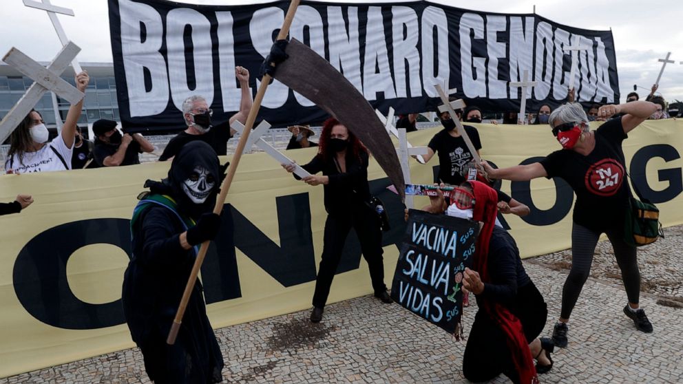 A demonstrator holds the Portuguese message "Vaccination saves lives", below, during a performance with a protester dressed as death and wearing a mock presidential sash, during a protest against President Jair Bolsonaro's handling of the COVID-19 pa