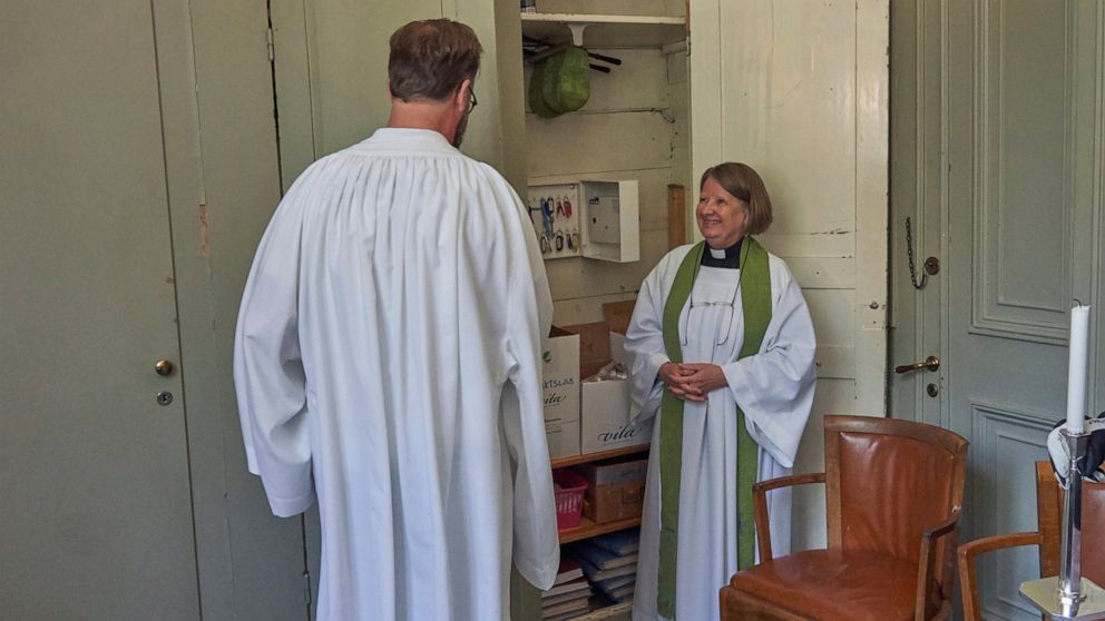 Rev. Elisabeth Oberg Hansen, right, of the Church of Sweden smiles to her student Rikard Kjellman as he puts on his clergy robes for the first time, ahead of his first sermon in Stockholm, Thursday, July 23, 2020. For the first time ever, there are m