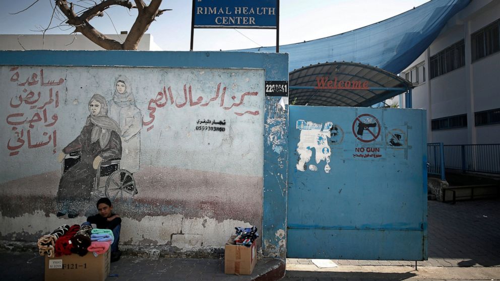 A Palestinian boy displays clothes for sale next to the entrance of the UNRWA Rimal Health Center in Gaza City, Monday, Nov. 9, 2020. The U.N. Relief and Works Agency for Palestinian refugees, known as UNRWA, said it needs to raise $70 million by the