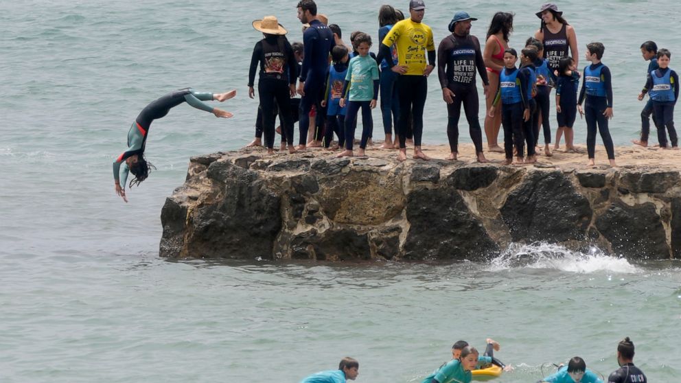 Young surf students dive from a pier at Carcavelos Beach, outside Lisbon, Tuesday, July 12, 2022. Portugal is experiencing a heatwave that led the government to declare a state of alert from Monday through Friday due to the heightened risk of forest 