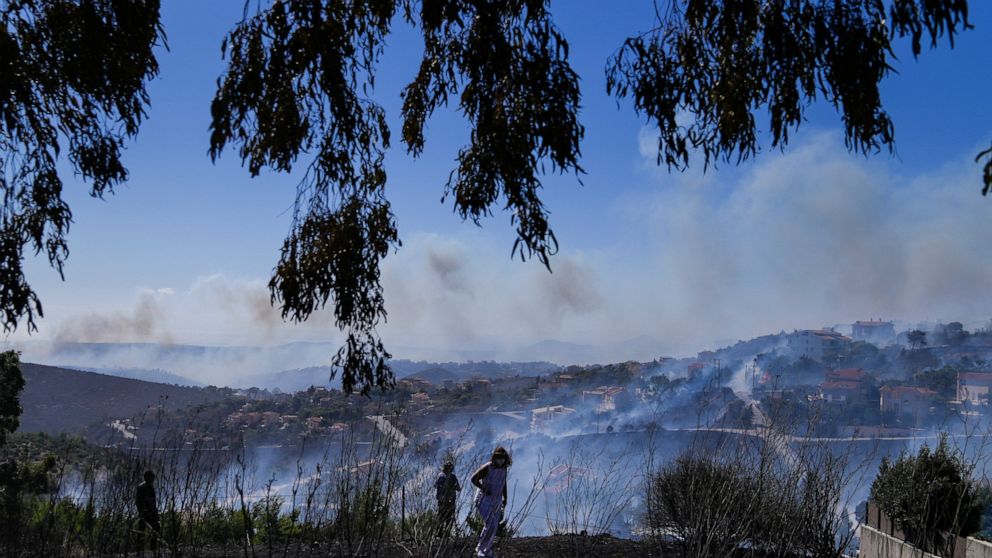 A woman walks in front of smoke from a fire in the area of Drafi , east of Athens on Wednesday, July 20, 2022. Hundreds of people were evacuated from their homes late Tuesday as a wildfire threatened mountainside suburbs northeast of Athens. Firefigh