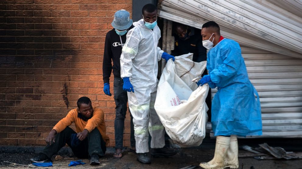 A family member watches on as police forensics officers carry the body his brother who was found inside a burned shop, in Johannesburg, South Africa, Sunday, July 11, 2021. Protests have spread from the KwaZulu Natal province to Johannesburg against 