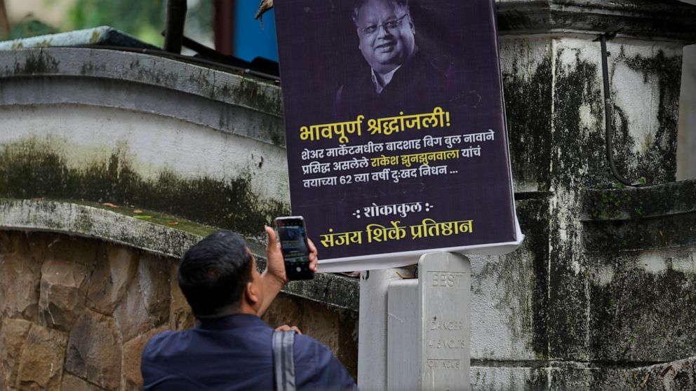 A man takes picture of a poster paying homage to veteran stock market investor and Indian billionaire Rakesh Jhunjhunwala displayed outside his residence, in Mumbai, India, Sunday, Aug.14, 2022. Jhunjhunwala, nicknamed India’s own Warren Buffett, die