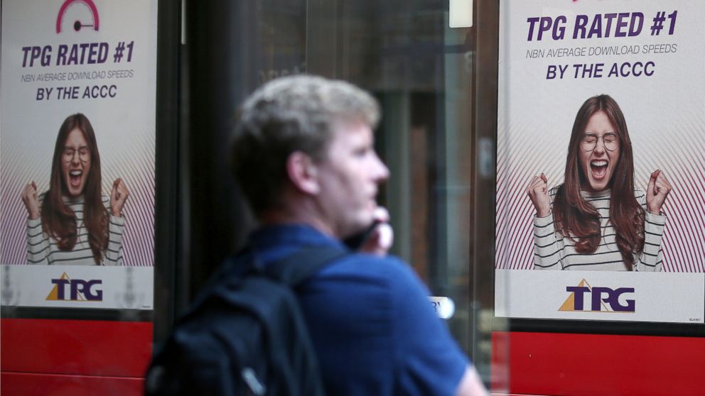 A bus branded with TPG ads goes past as a man uses his phone at a bus stop in Sydney, Tuesday, Jan. 29, 2019. TPG Telecom said it had abandoned the rollout of what would have been Australia's fourth mobile network because of the government's ban on C