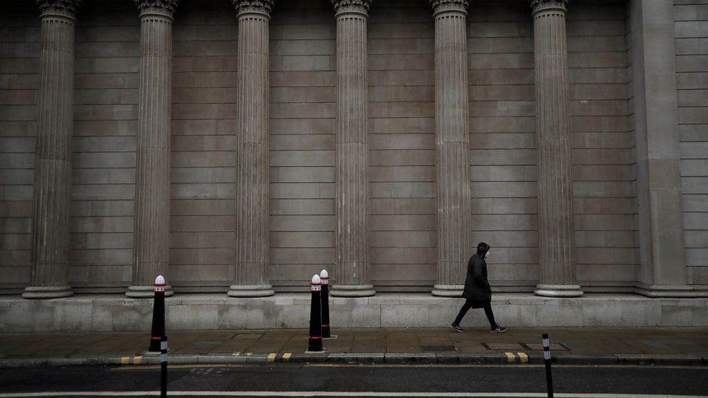 FILE - In this Jan. 5, 2021 file photo, a man wearing a face mask to curb the spread of coronavirus walks past part of the Bank of England in the City of London financial district, on the first morning of England entering a third national lockdown si