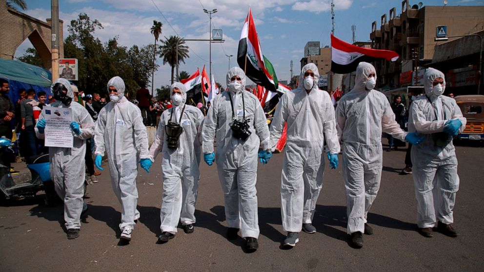 FILE - In this March 1, 2020 file photo, anti-government protesters wear hazmat-like suits and gas masks during a rally in Baghdad, Iraq. As 2019 gave way to 2020 in a cloud of tear gas, and in some cases a hail of bullets, from Hong Kong to Baghdad,