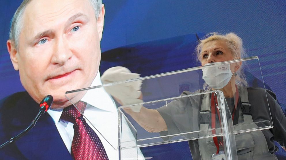 FILE - A worker cleans a speaker's podium as Russian President Vladimir Putin seen on a screen in the background at the St. Petersburg International Economic Forum in St. Petersburg, Russia, June 4, 2021. Russia’s showpiece investment gathering begin