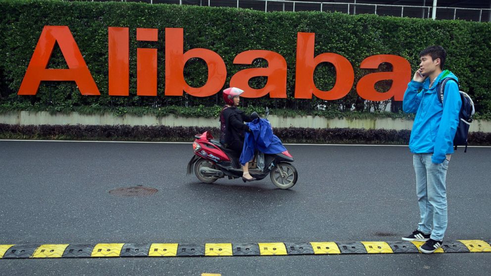 FILE - In this May 27, 2016, file photo, a man talks on his phone as a woman rides on an electric bike past a company logo at the Alibaba Group headquarters in Hangzhou in eastern China's Zhejiang province. Chinese authorities summoned 11 companies i