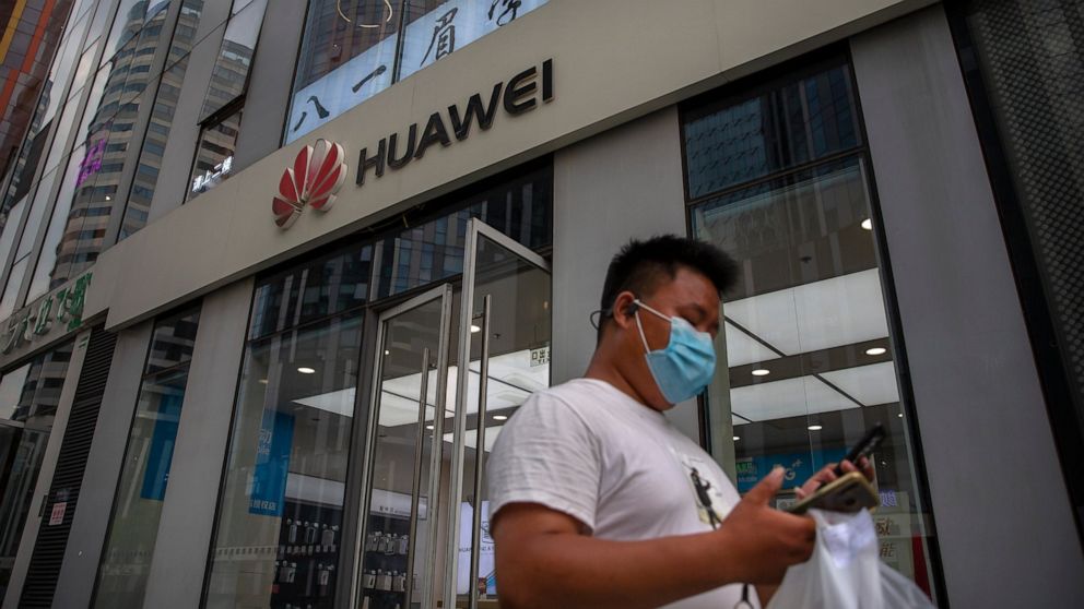FILE - In this Wednesday, July 1, 2020 file photo, a man wearing a face mask to protect against the new coronavirus looks at his smartphone as he walks past a Huawei store in Beijing. The British government is reportedly poised to backtrack on plans 