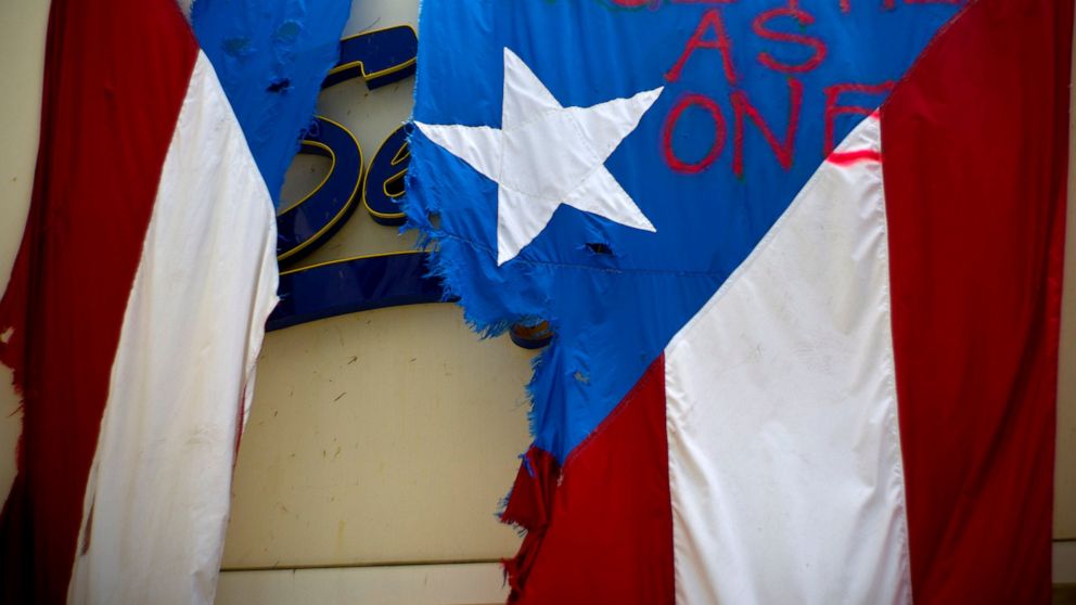 FILE - In this Sept. 27, 2017 file photo, a ripped Puerto Rican national flag spray painted with the words "Together as One" hangs from the facade of a business, in San Juan, Puerto Rico. A federal control board that oversees Puerto Rico's finances f