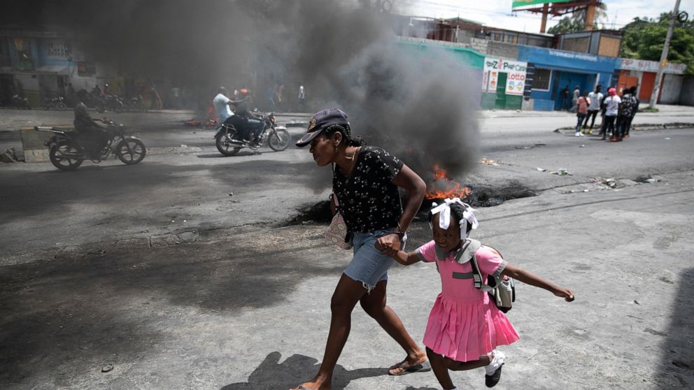 A woman guides a child past a demonstration against increasing violence in Port-au-Prince, Haiti, Tuesday, March 29, 2022. The protest coincides with the 35th anniversary of Haiti’s 1987 Constitution and follows other protests and strikes in recent w