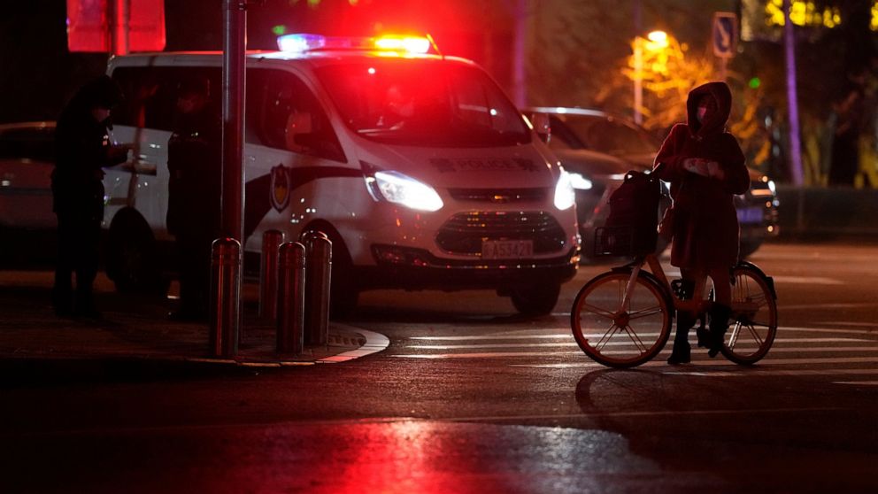A passerby on a bicycle stops near a police van monitoring an area where protesters were expected to gather in Beijing, Monday, Nov. 28, 2022. Chinese authorities eased some anti-virus rules but affirmed their severe 