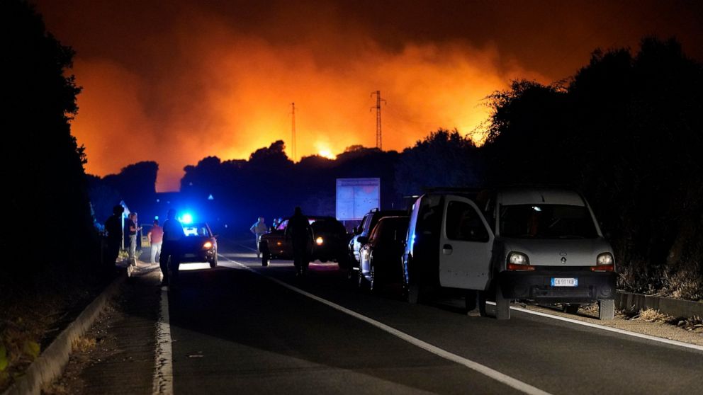 Cars are parked by the road as fires have been raging through the countryside in Cuglieri, near Oristano, Sardinia, Italy, early Sunday, July 25, 2021. Hundreds of people were evacuated from their homes in many small towns in the province of Oristano