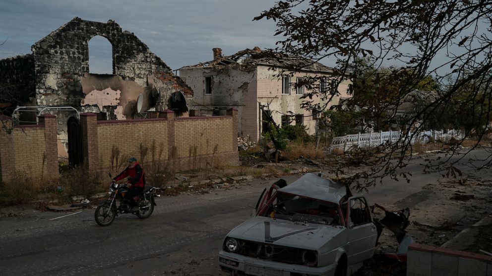A man drives his motorcycle past a destroyed car in the retaken village of Velyka Oleksandrivka, Ukraine, Wednesday, Oct. 12, 2022. (AP Photo/Leo Correa)