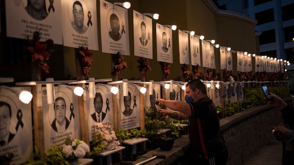 Javier Casana leaves flowers on the portrait of his uncle Jorge Luis Casana, 62, a doctor who died from COVID-19, in Lima, Peru, Tuesday, January 19, 2021. The Peruvian Medical College reported that at least 11 doctors have died during the first days