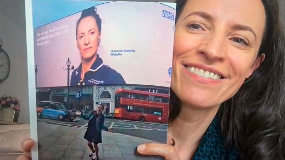 In this image taken from an online video interview with The Associated Press, Claudia Anghel, a Romanian midwife working in England, holds up a photograph of a large display in Piccadilly Circus showing her portrait shot by celebrity photographer Ran