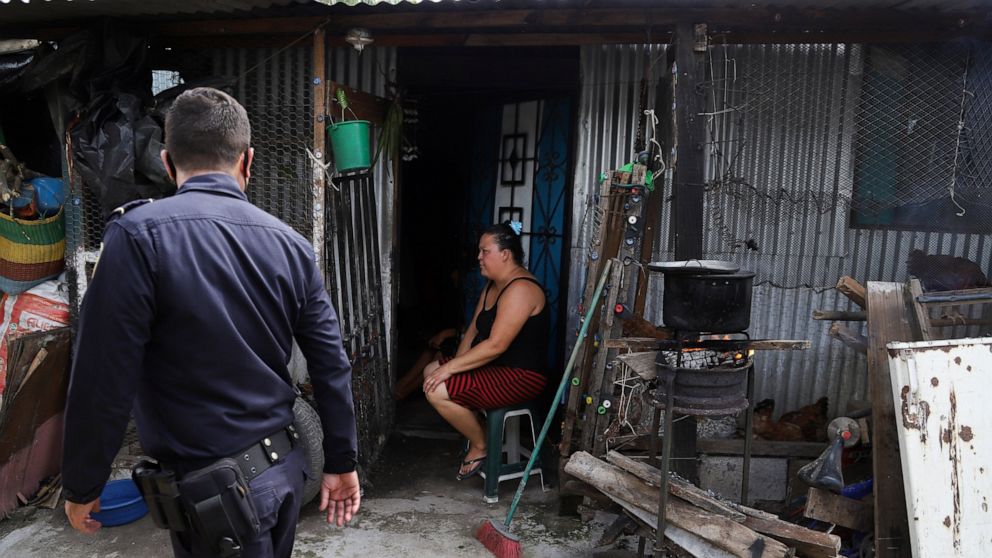 A woman sits outside her home as a police officer patrols in the Kiwanis community in Soyapango, El Salvador, Tuesday, Aug. 16, 2022. The government of Salvadoran President Nayib Bukele asked Congress on Tuesday to approve a fifth extension of the st