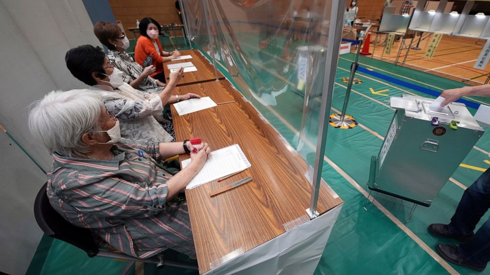Staff members of a local election administration commission, wearing face masks, observe a voter cast a ballot in the upper house elections at a polling station Sunday, July 10, 2022, in Tokyo. (AP Photo/Eugene Hoshiko)