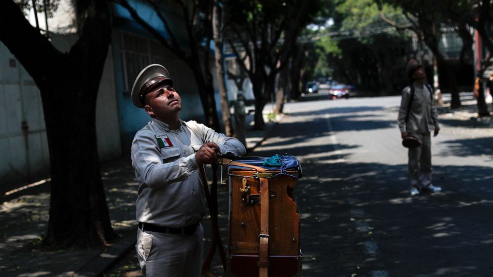 FILE - Sergio Munoz turns the crank on a traditional organ, as his assistant looks for residents in their homes willing to donate a few pesos, in the Roma Norte neighborhood of Mexico City, April 18, 2020. Mexico’s economy slowed in the third quarter